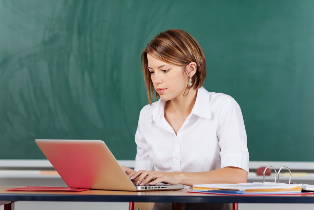 Young teacher browsing the internet through laptop inside the classroom