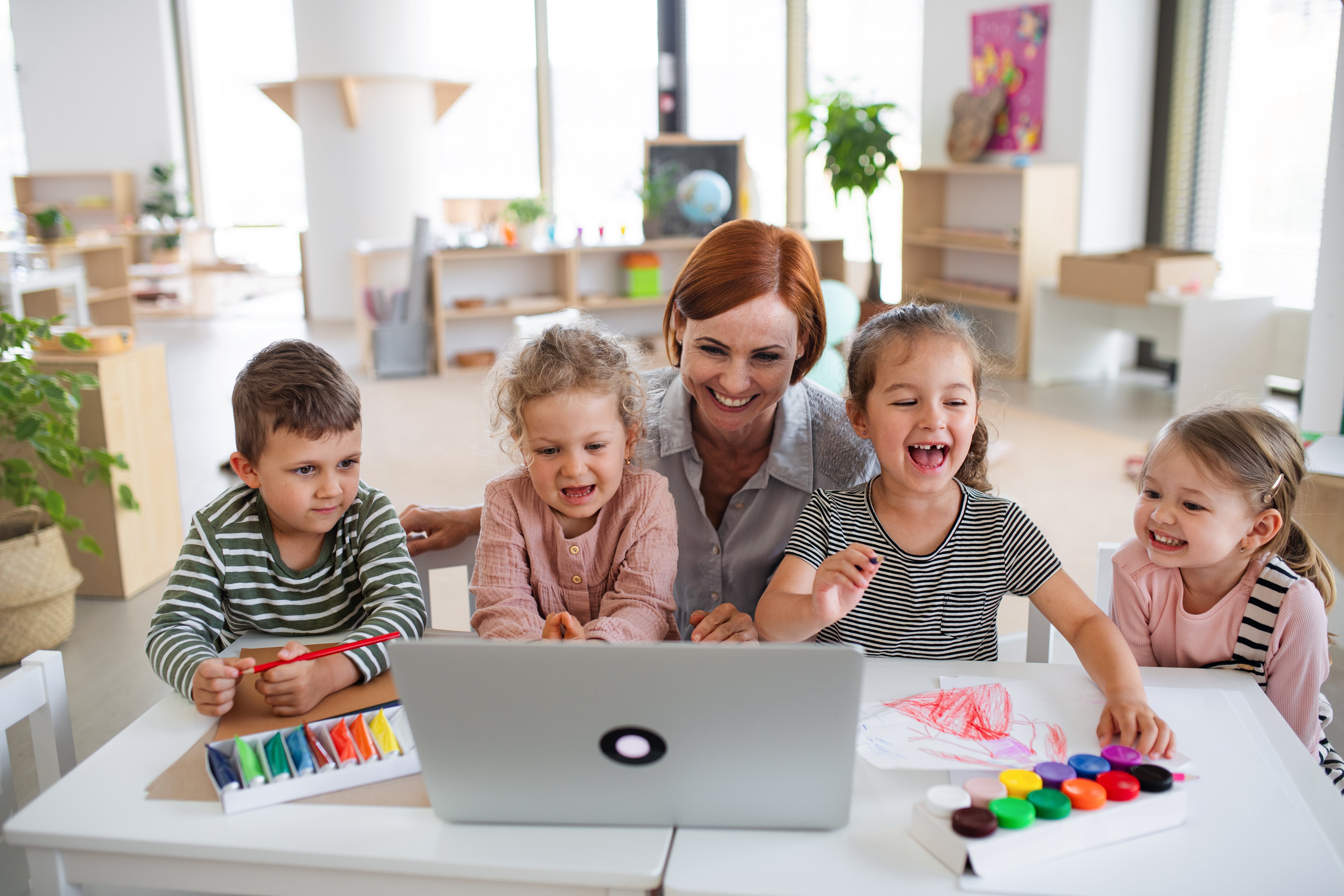 group-small-nursery-school-children-with-teacher-indoors-classroom-using-laptop