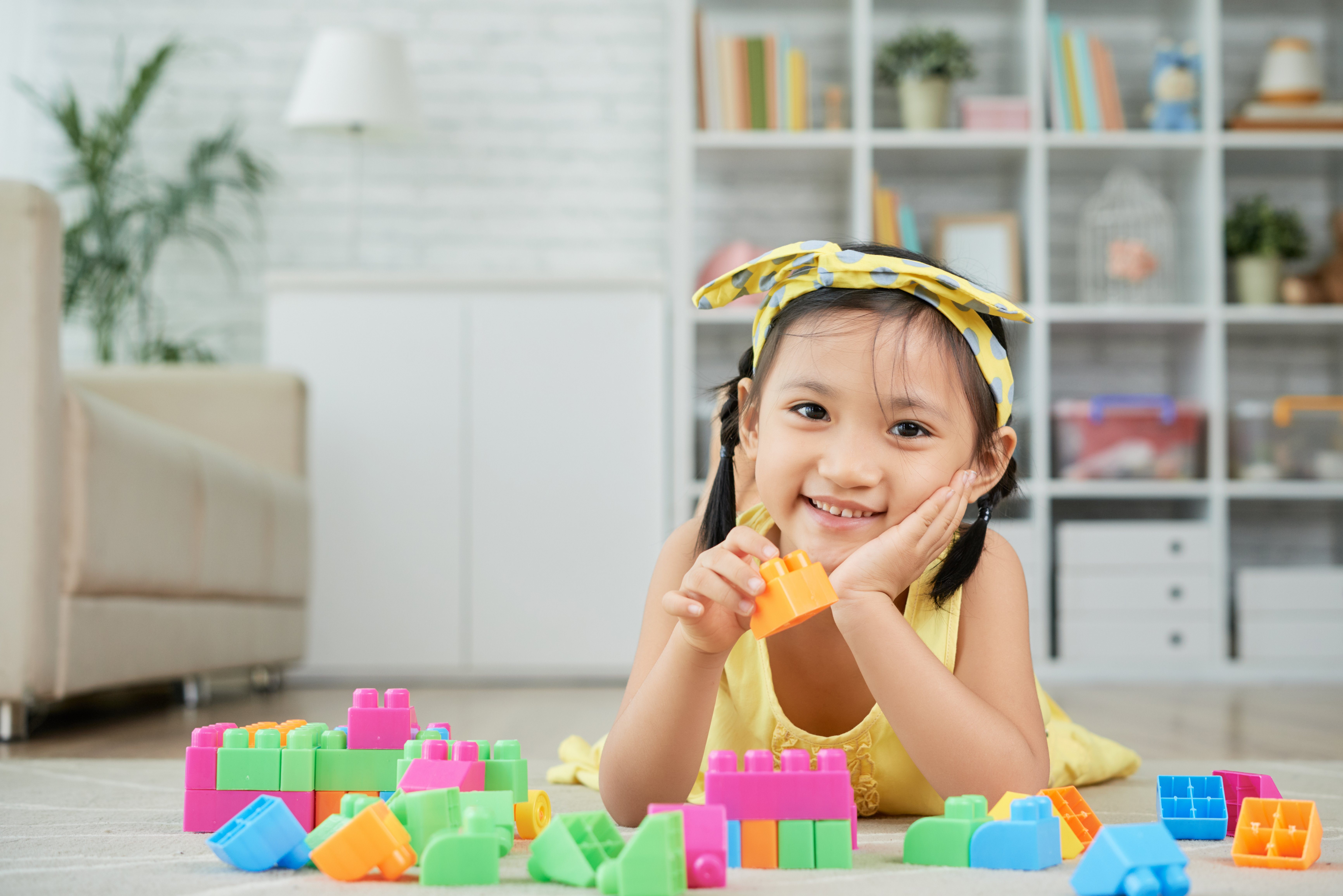 little-asian-girl-lying-floor-home-playing-with-colorful-building-blocks