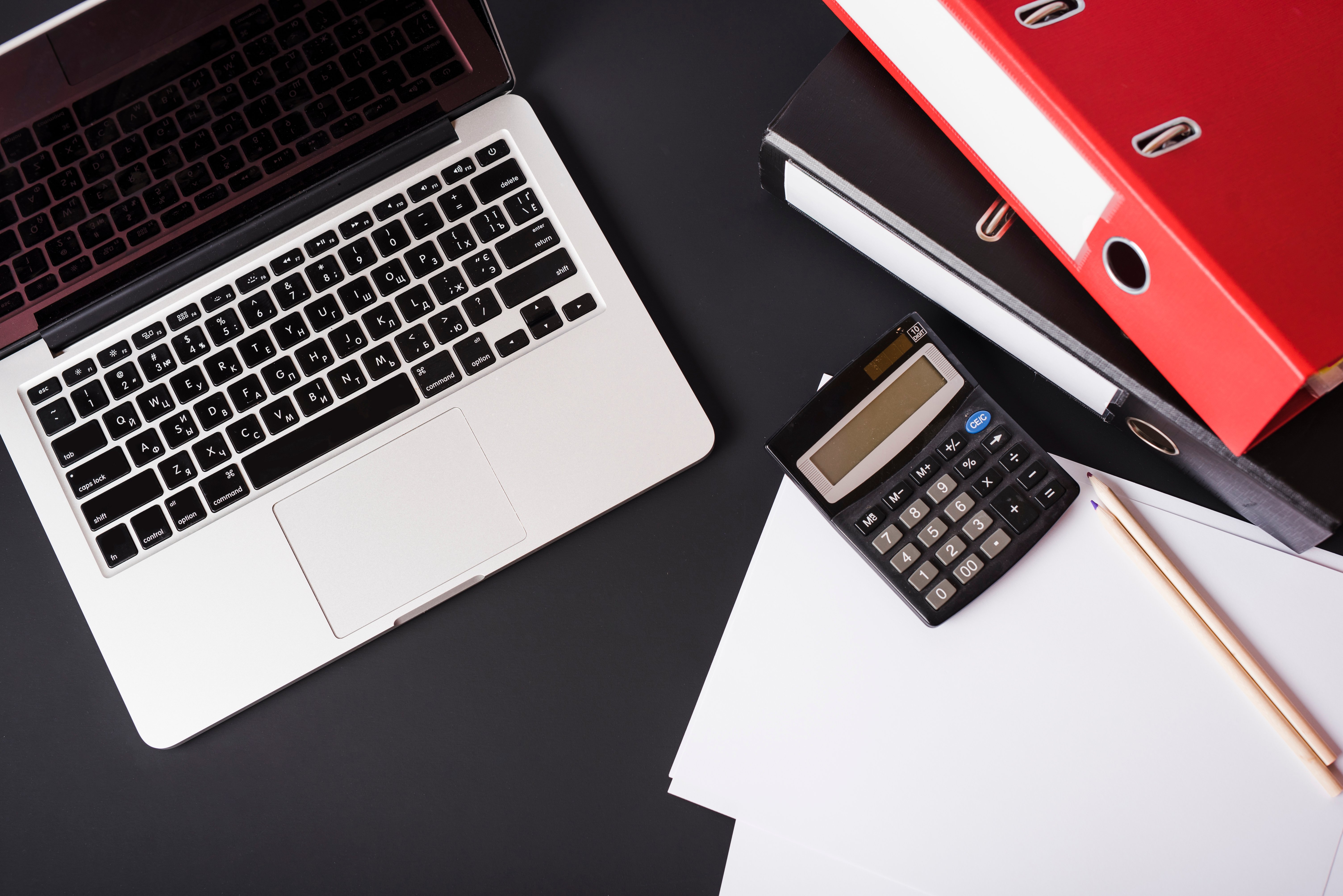 overhead-view-laptop-file-folders-calculator-pencils-paper-black-background